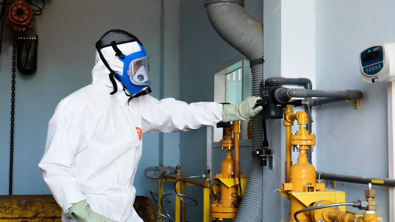 Specialist in a protective coverall and full-face respirator taking measurements at an industrial installation